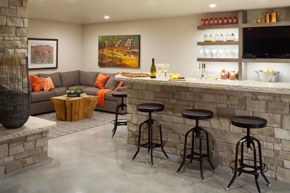 Basement bar and lounge with a stone-front bar, bar stools, an orange sectional and a wall TV