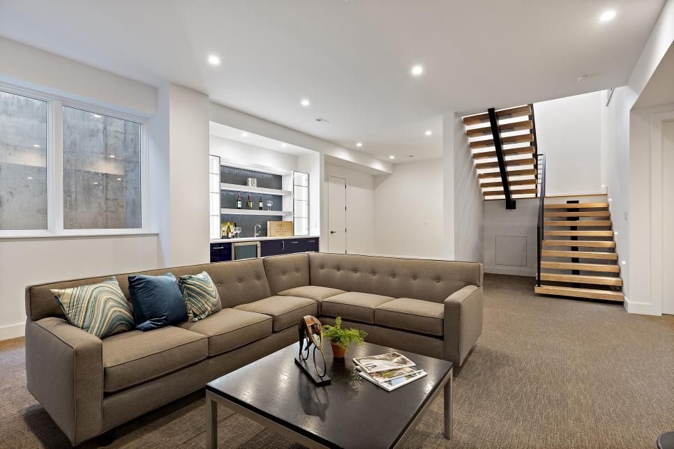 Finished basement lounge with a grey sectional and a floating wood staircase
