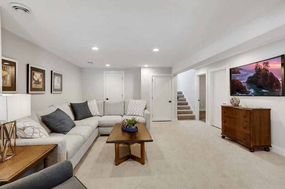 Bright basement living room with a grey sectional, wood coffee table, framed art and a staircase