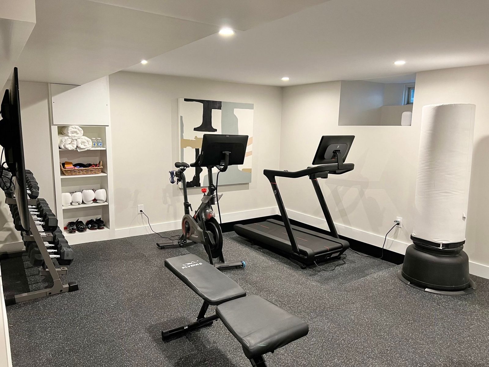 Basement home gym with a treadmill, exercise bike, free weights and a training screen